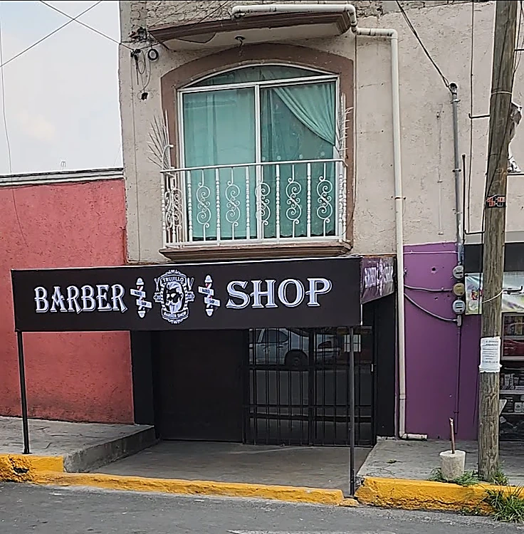 Fachada de Barber Shop Trujillo: letrero negro con las letras BARBER SHOP y el logo, bajo un balcón con herrería blanca