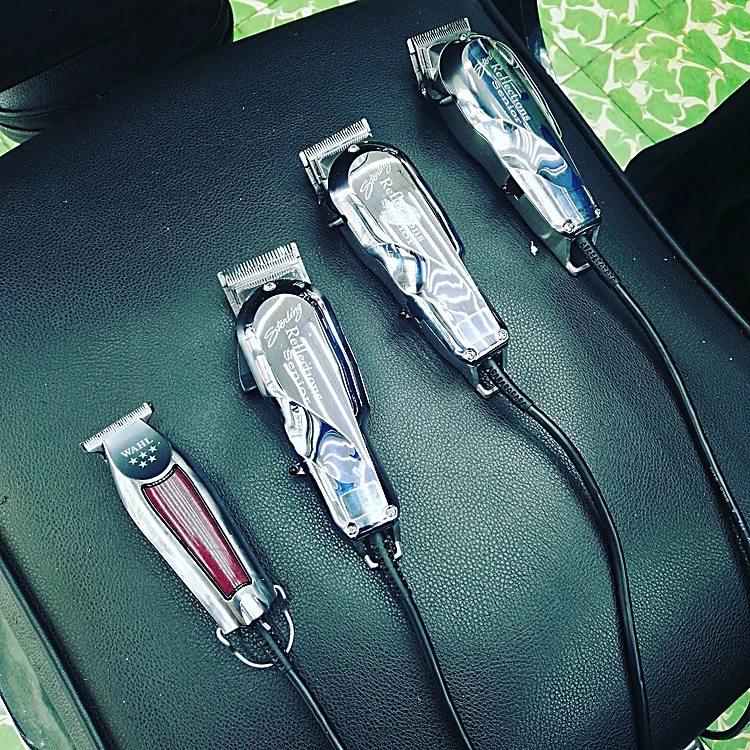 Cuatro máquinas de corte cromadas, tres clippers y una trimmer, alineadas sobre un sillón de cuero negro