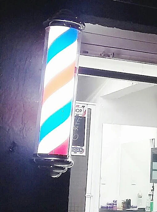 Poste de barbero encendido con franjas azul, coral y blanco en la entrada, de noche