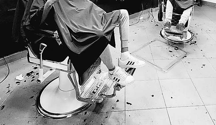 Foto en blanco y negro de la base cromada de un sillón de barbero con pelo recién cortado en el piso